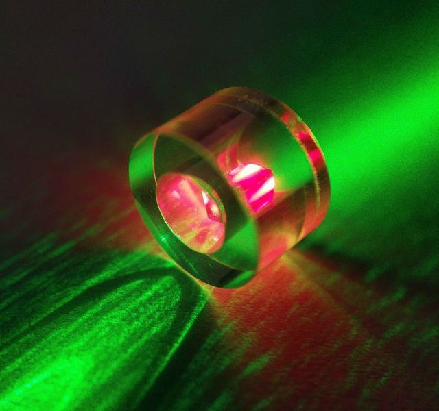 A sapphire ring resonator lying on its side, with a diamond fluorescing red in the bore