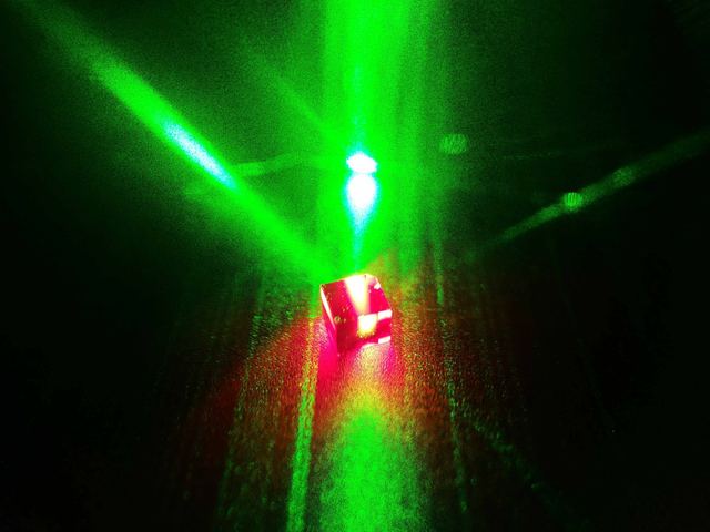 A diamond sample fluorescing red beneath a vertical green pump beam