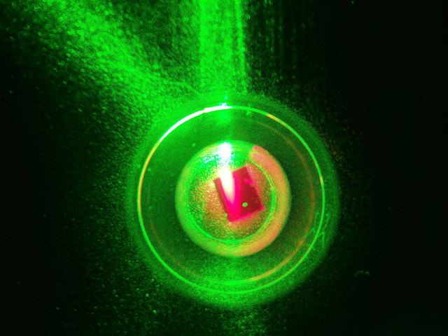 Concentric rings of scattered green laser light around a diamond sample, viewed down the resonator axis