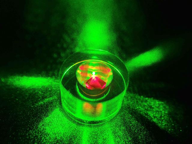 A diamond sample glowing red inside a sapphire ring resonator, under green pump laser light